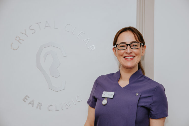 Rebecca Shields, posing in front an a Crystal Clear Ear Clinic logo
